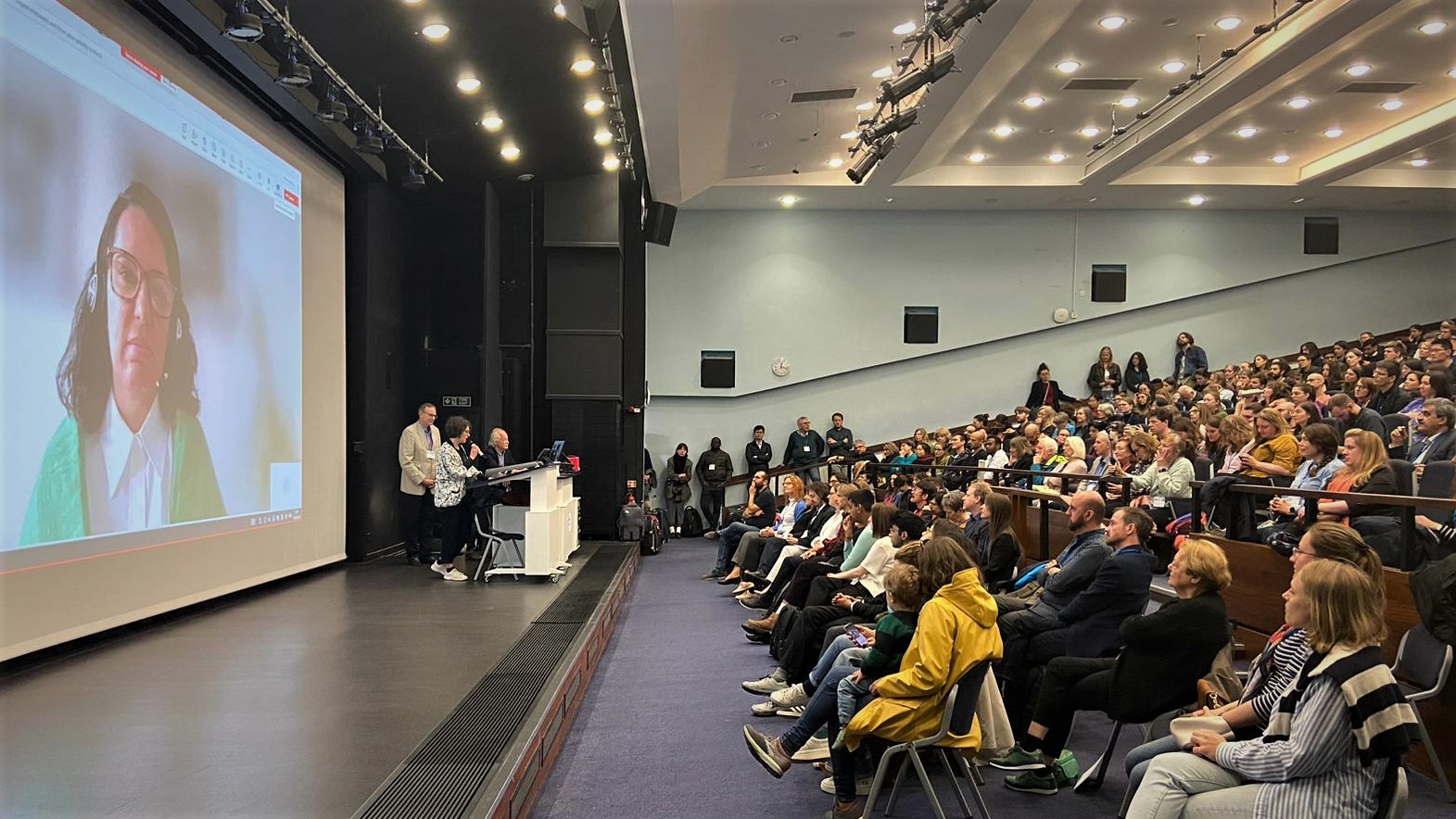 Auditorium with a full audience. Dr. Vono de Vilhena is shown on screen