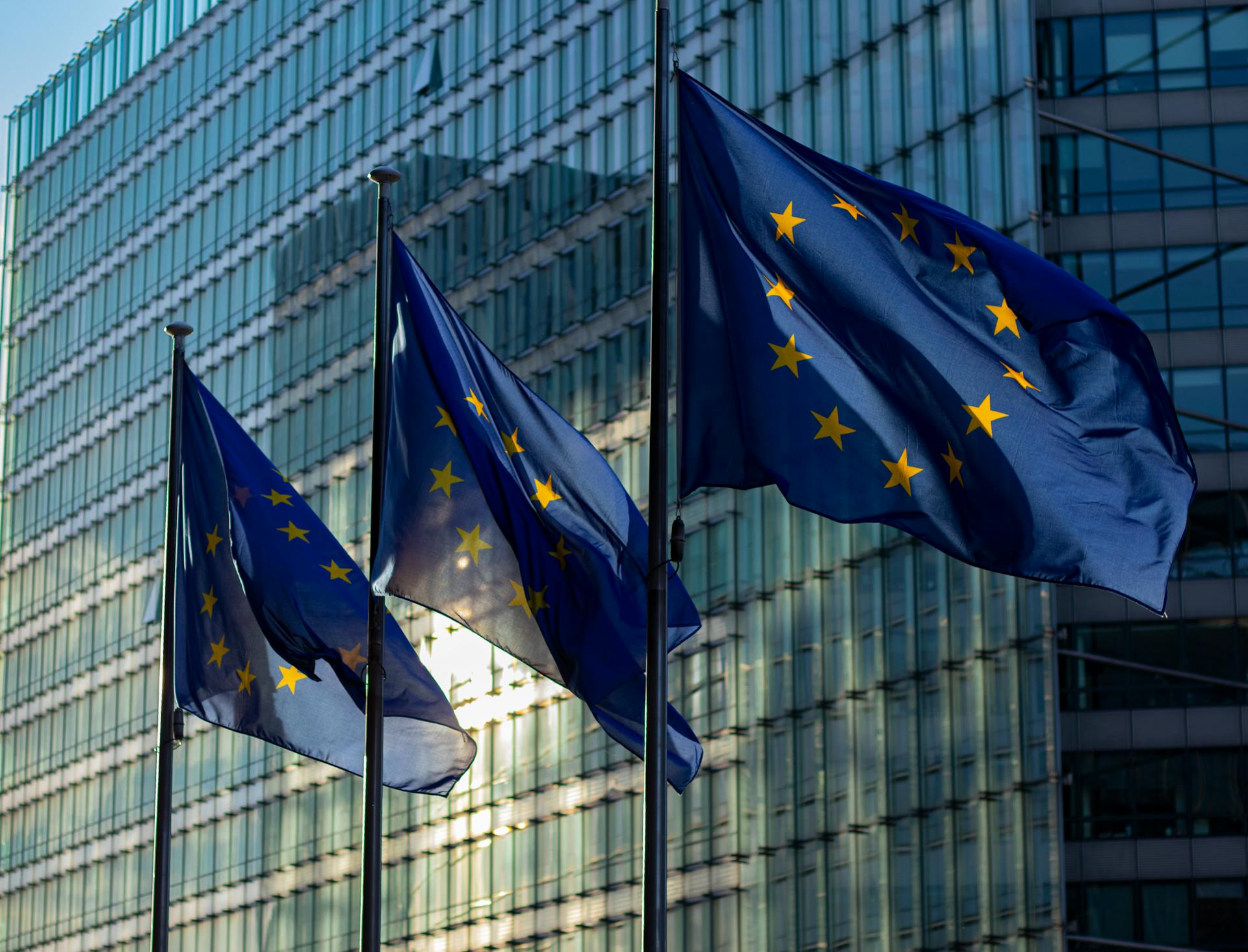 EU flags waving in front of a glass building at sunrise