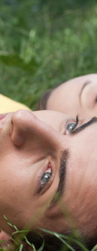 A young man and woman lying in the grass, looking pensive