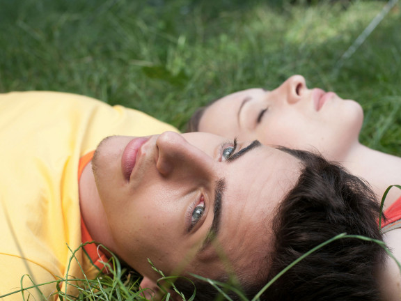 A young man and woman lying in the grass, looking pensive