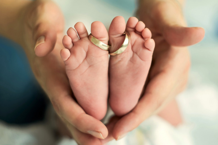 Baby foots and wedding rings in the hands of the mother