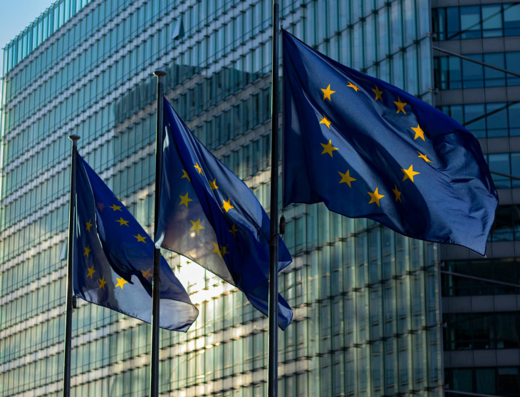 EU flags waving in front of a glass building at sunrise